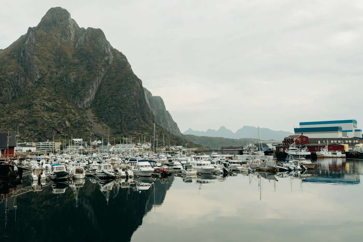 Yachthafen voller kleiner Boote auf stillem Wasser unter einem steilen Gipfel, bedeckter Himmel