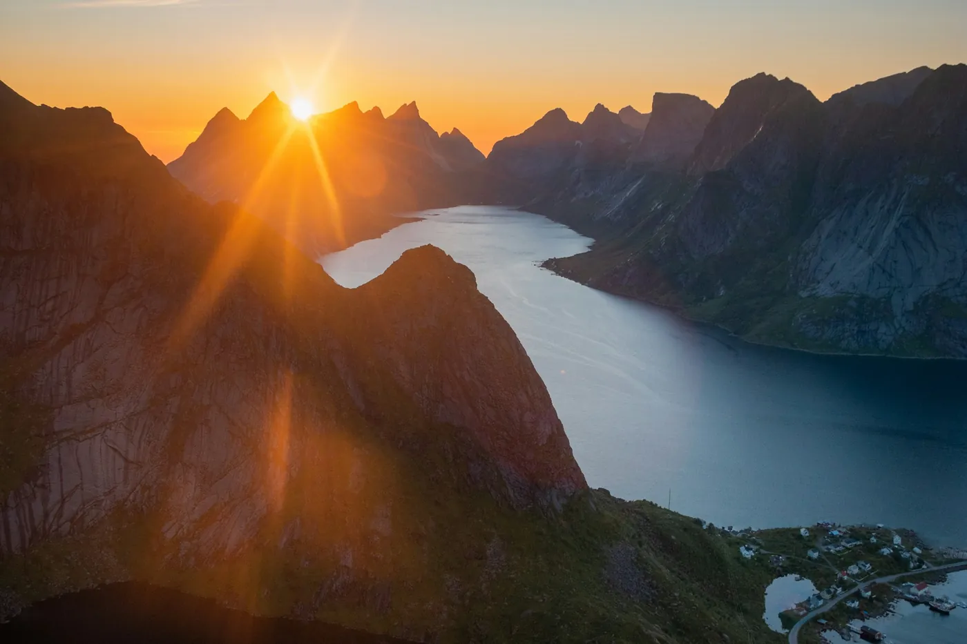 Soleil bas en étoile au-dessus de sommets déchiquetés et d’un fjord, vus d’en haut