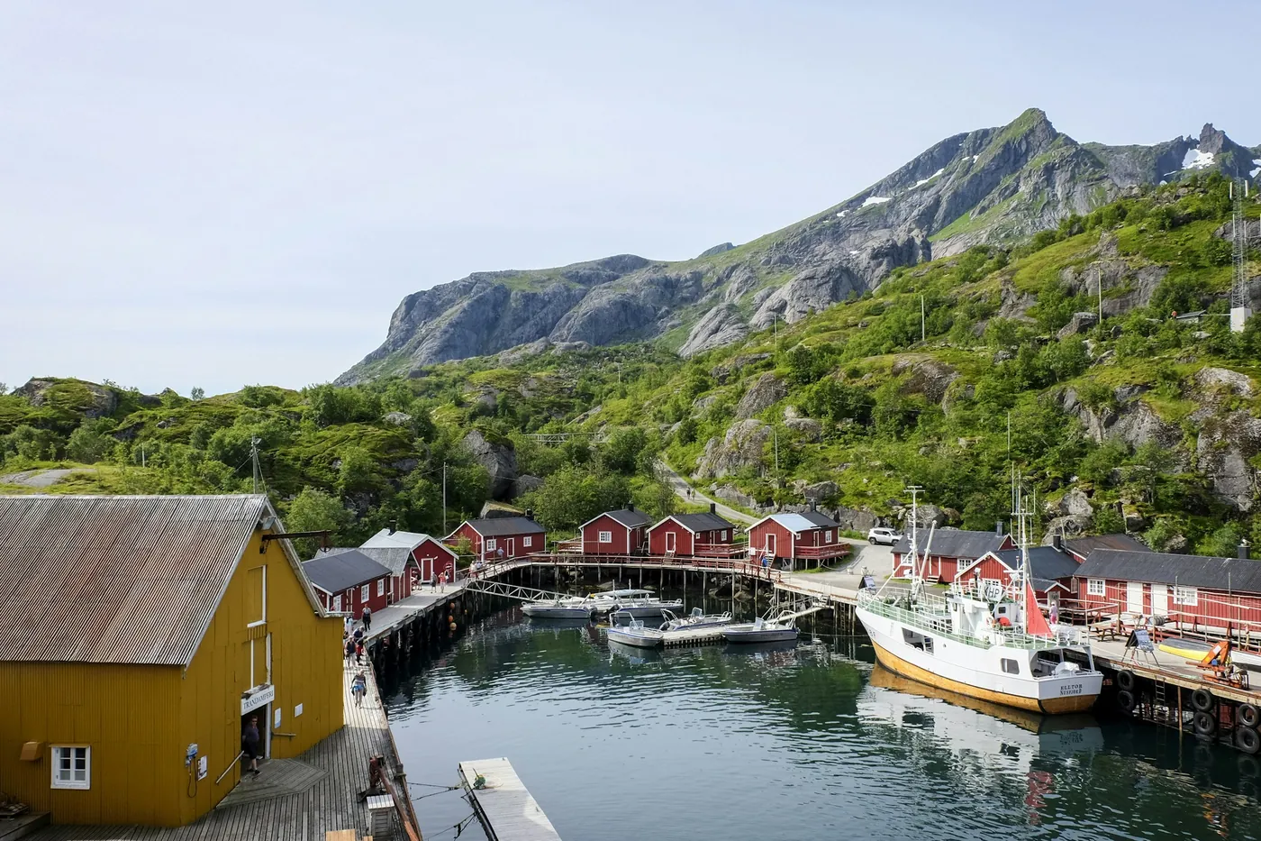 Petit port avec des bâtiments en bois jaunes et rouges, des bateaux et des collines vertes