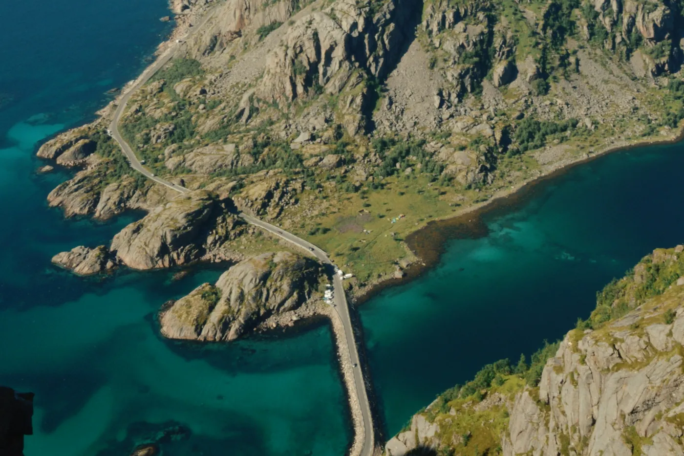 Vista aérea de una carretera que recorre una costa rocosa hasta un puente sobre aguas turquesa