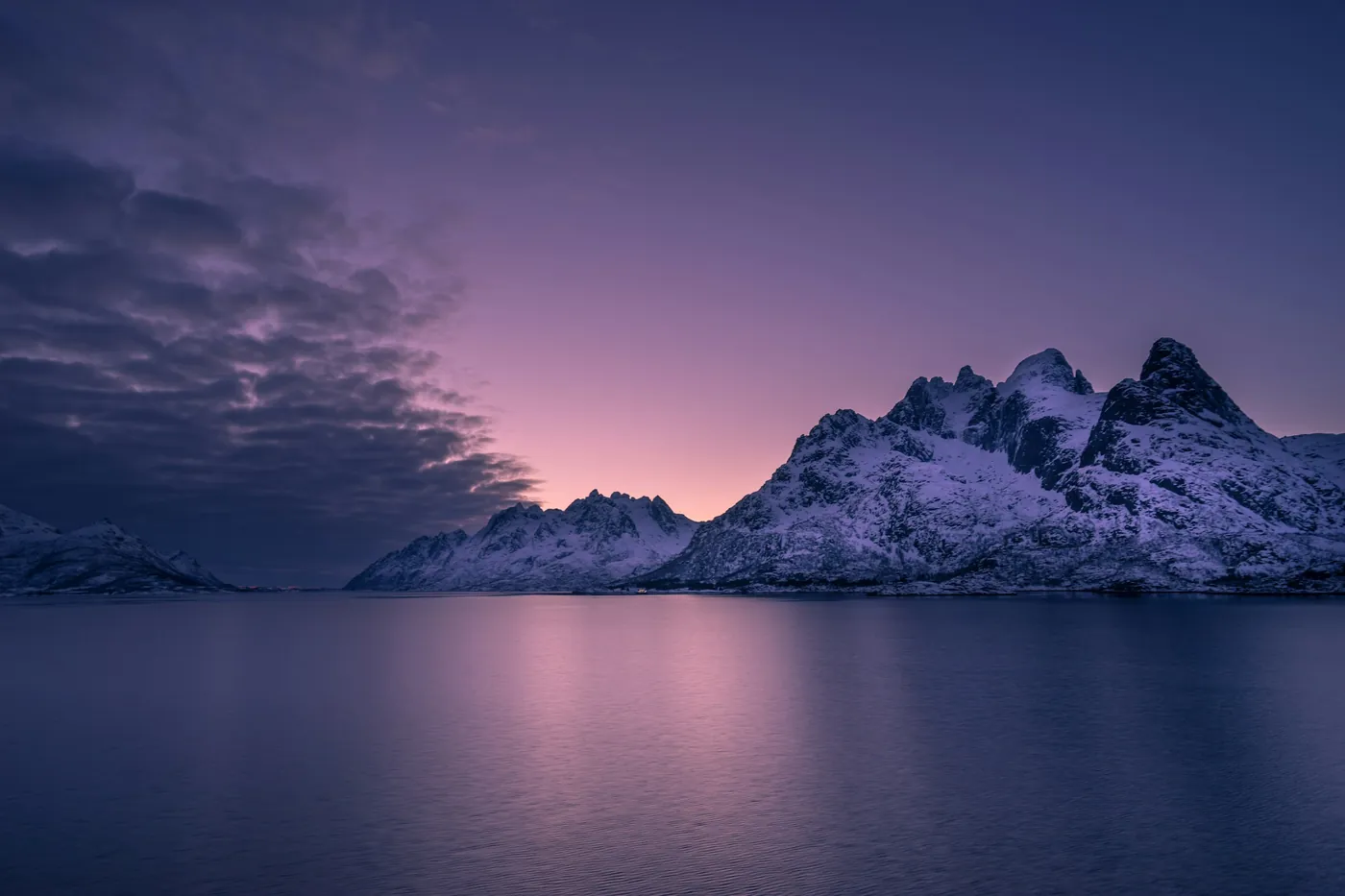 Schneebedeckte Berge unter einem rosa und violetten Dämmerungshimmel, der sich im ruhigen Meer spiegelt